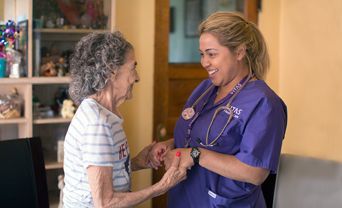 A female senior citizen holds hands with a VITAS team member