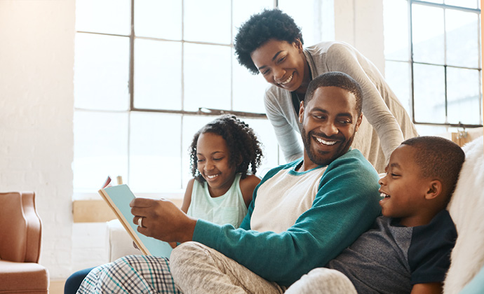 A family of four gathers on a sofa at their home