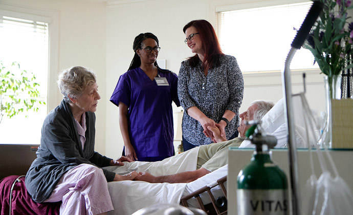A man lying in bed is surrounded by his wife, daughter and VITAS hospice nurse