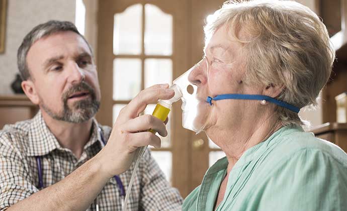 A respiratory therapist helps a patient with an oxygen mask