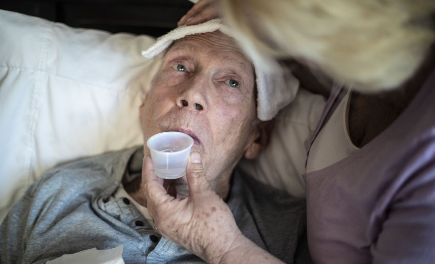 A caregiver lifts a small medicine cup to her patient's lips