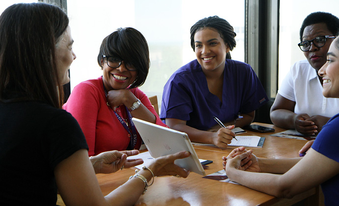 Healthcare professionals talk at a conference table while one shows information on a tablet