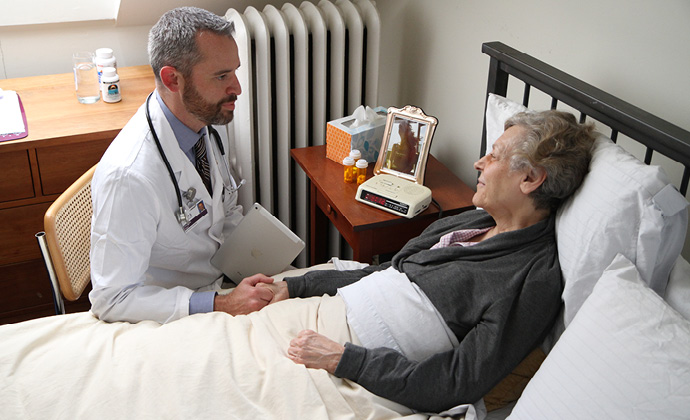 A physician talks with and holds the hand of a woman who is lying down in bed