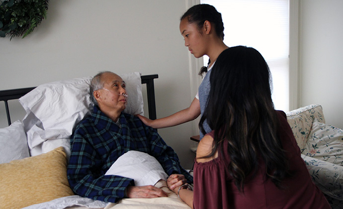 A man sitting up in bed at home talks to his two grandchildren