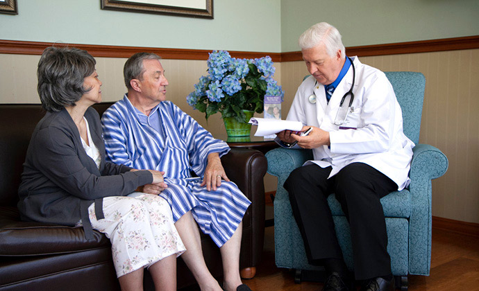 A husband and wife sit on a sofa and talk with a physician
