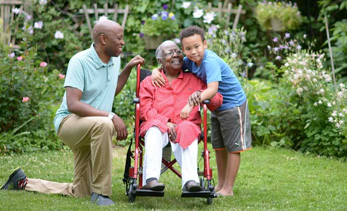 A woman seated in a wheelchair embraces her grandson as they enjoy time in an outdoor garden